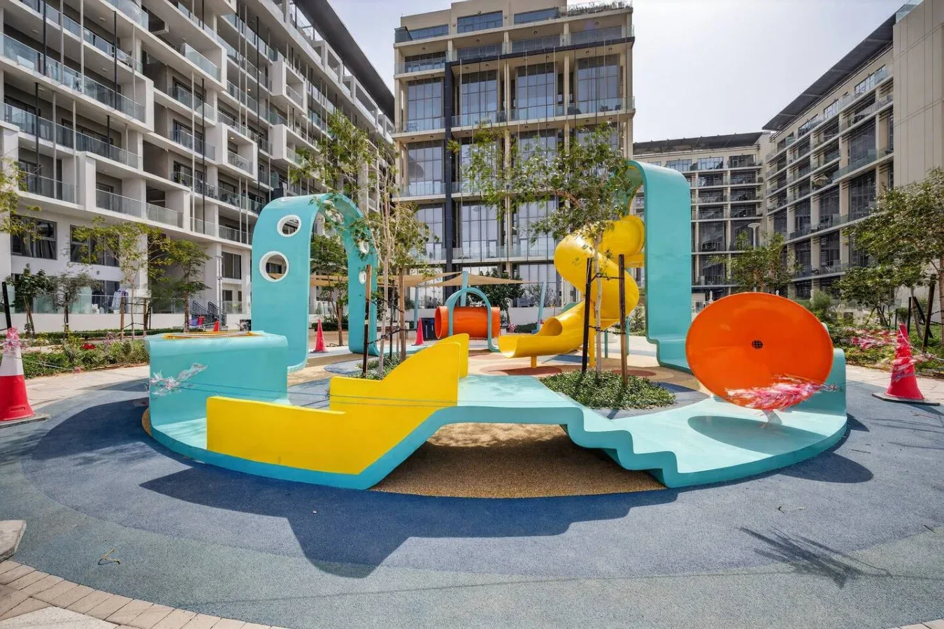 A colorful outdoor playground with slides sits in a courtyard surrounded by apartment buildings.
