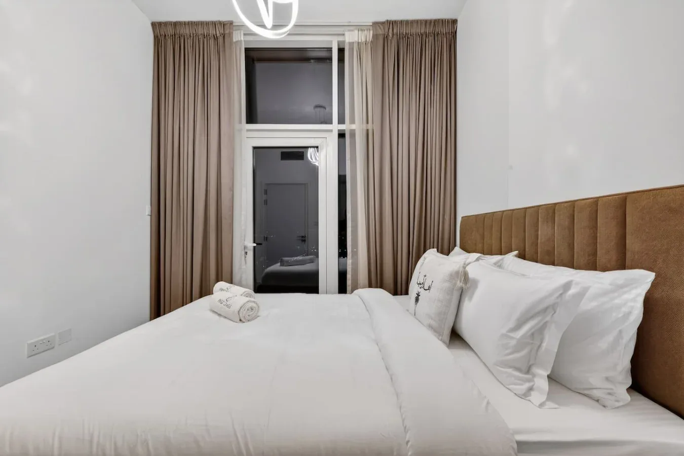 A bedroom with a neatly made bed and tall curtains beside the window.