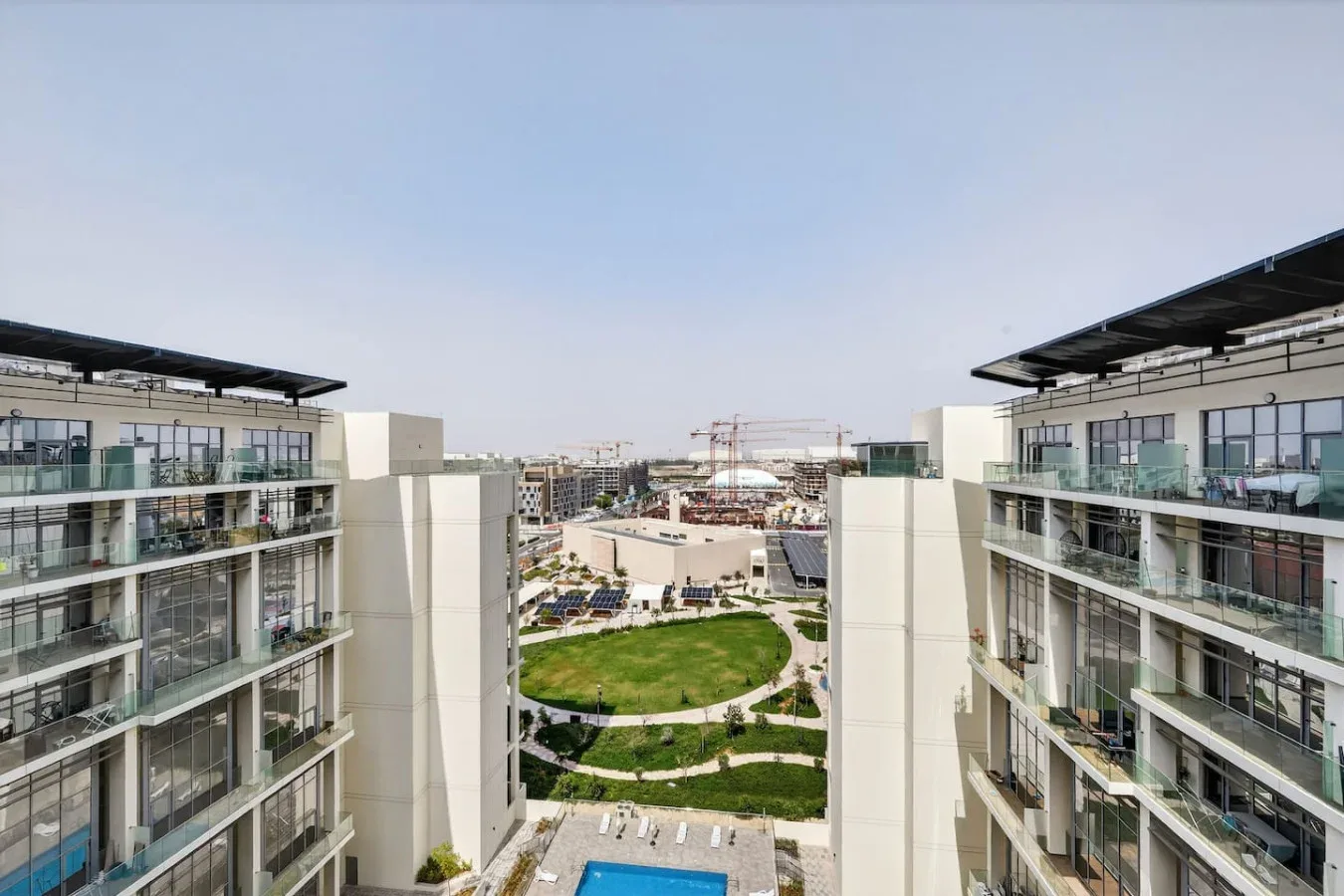 Modern apartment buildings overlook landscaped grounds and a swimming pool.