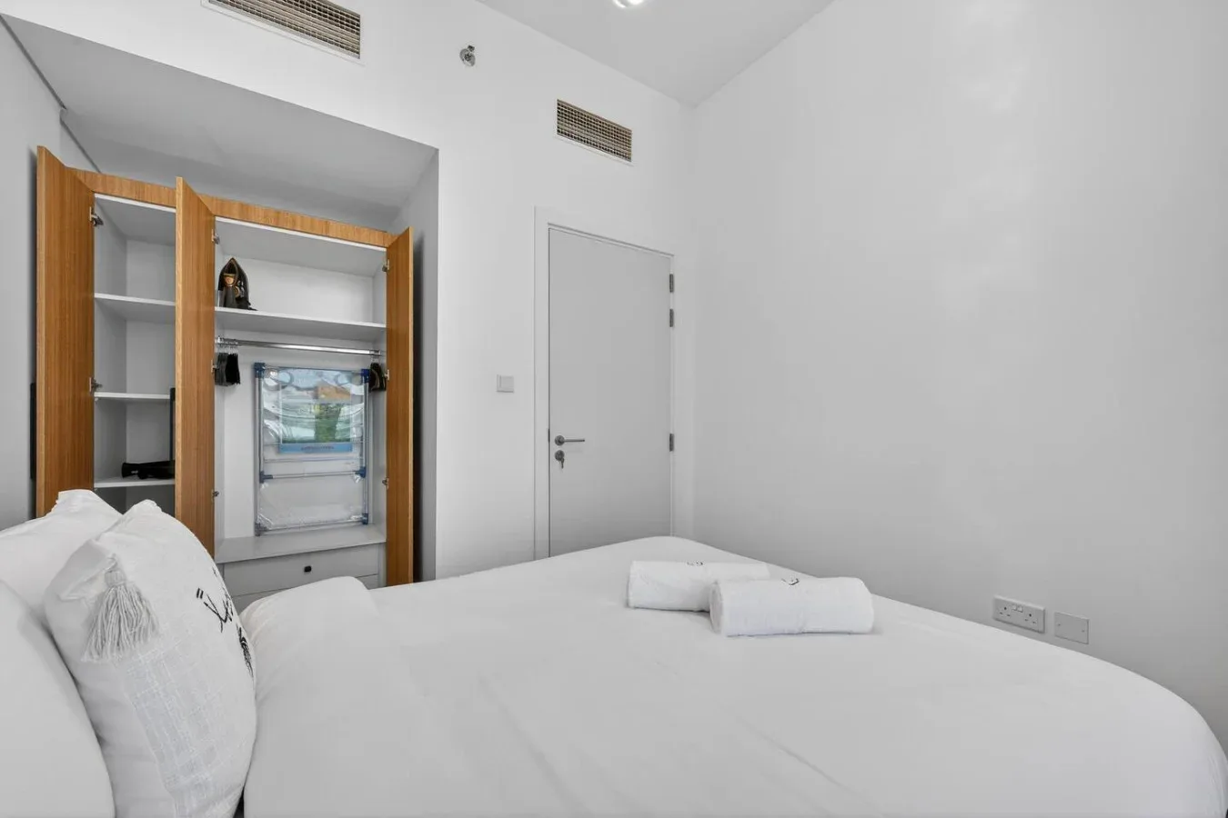 A bright bedroom with a neatly made bed and an open wardrobe.