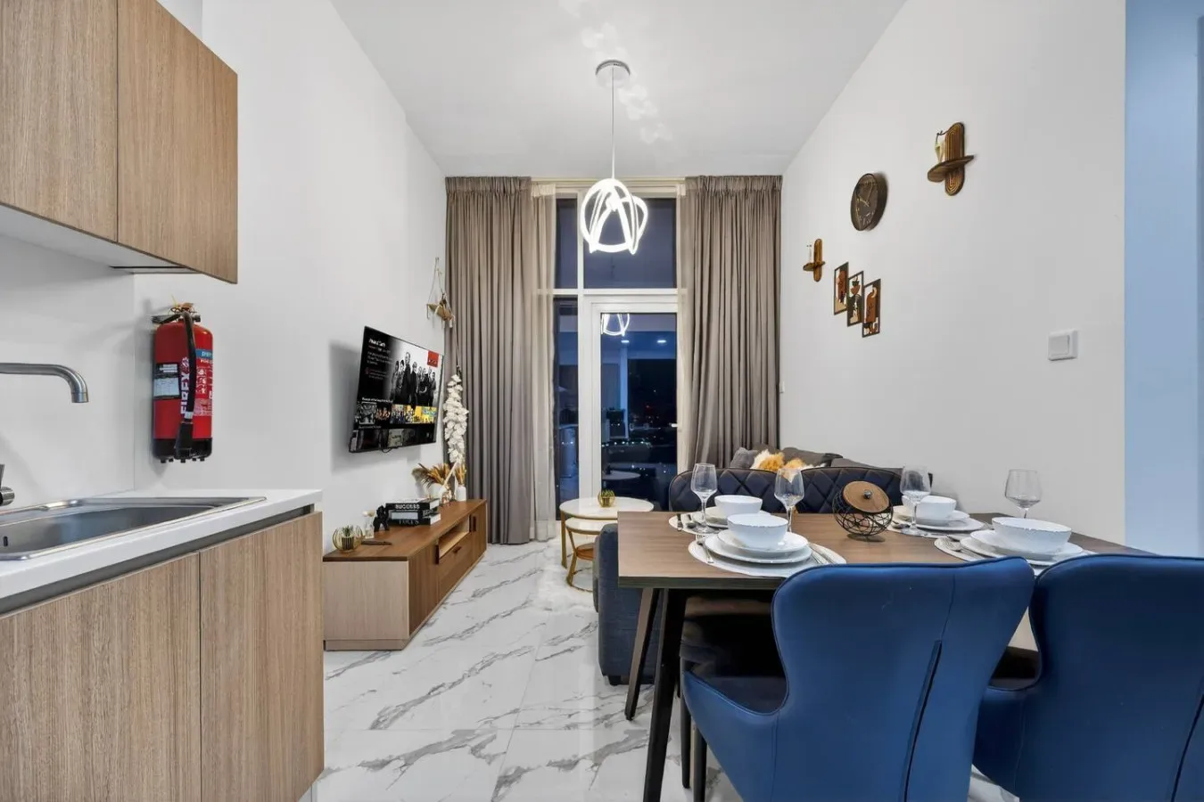 A living and dining area with a table, blue seating, and tall curtained windows.