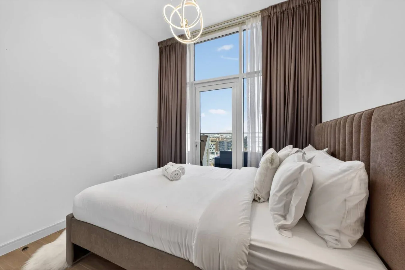 A bright bedroom with a white bed, tall windows, and dark curtains.