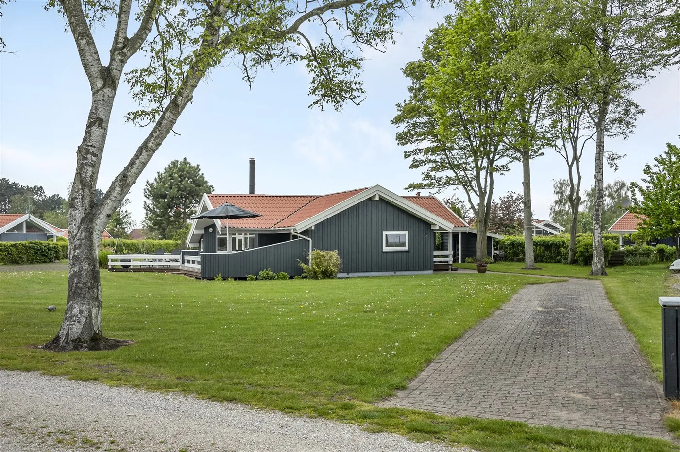 A dark house with a red roof stands beside a paved driveway and green lawn.