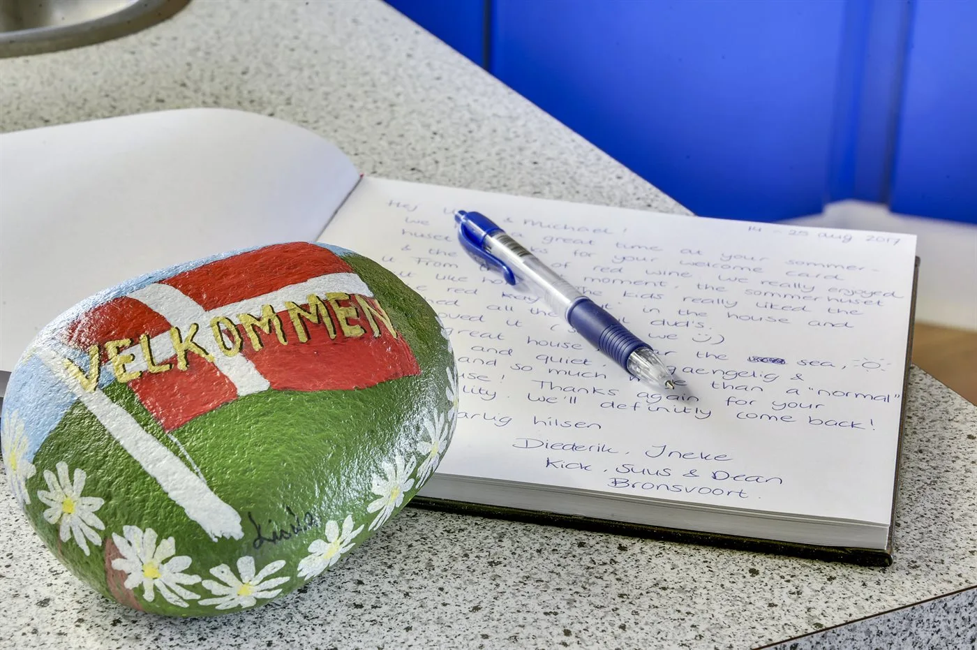 A painted stone rests beside an open guestbook and pen on a countertop.