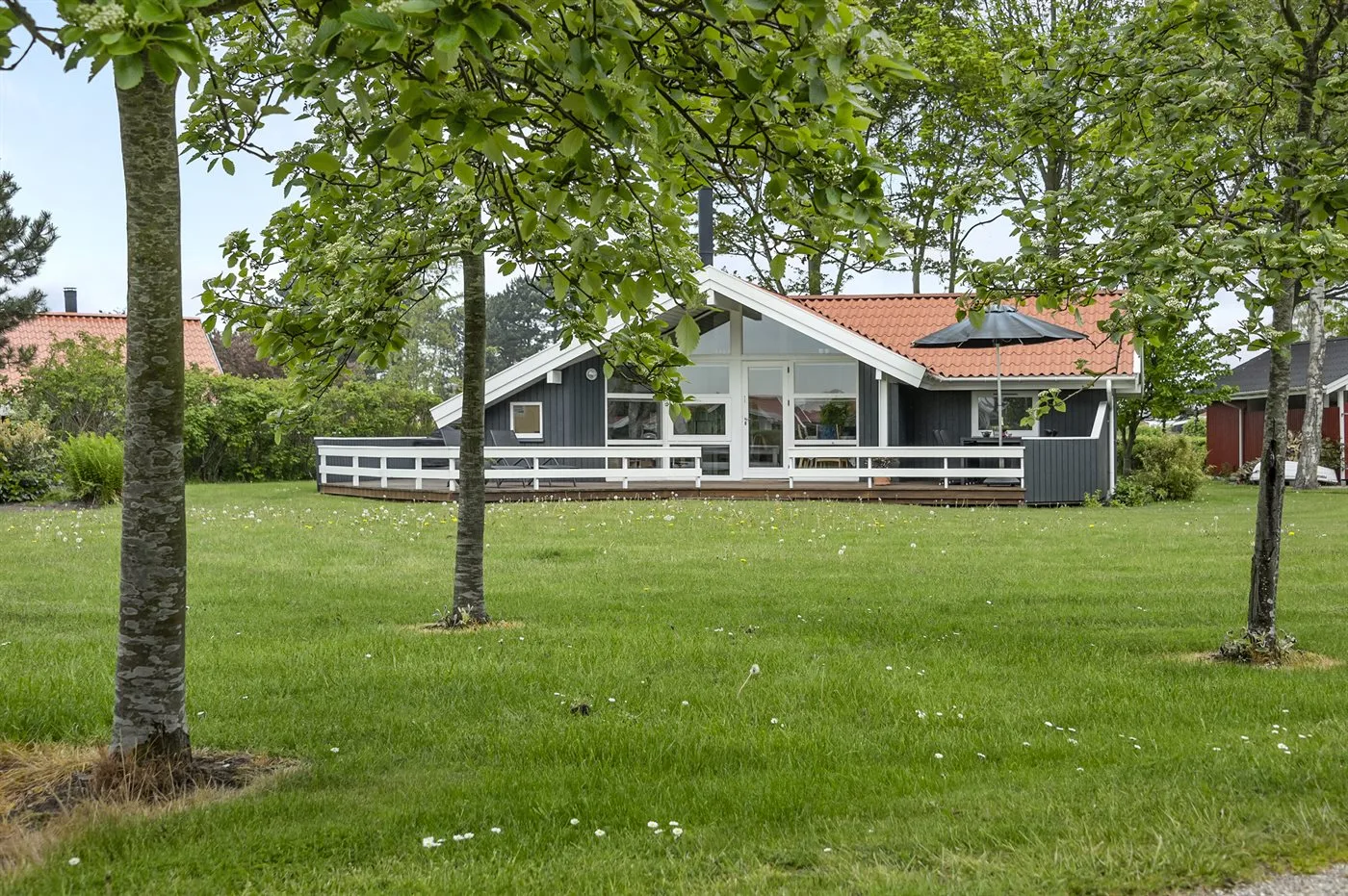 A low house with a white porch stands beyond a grassy lawn.