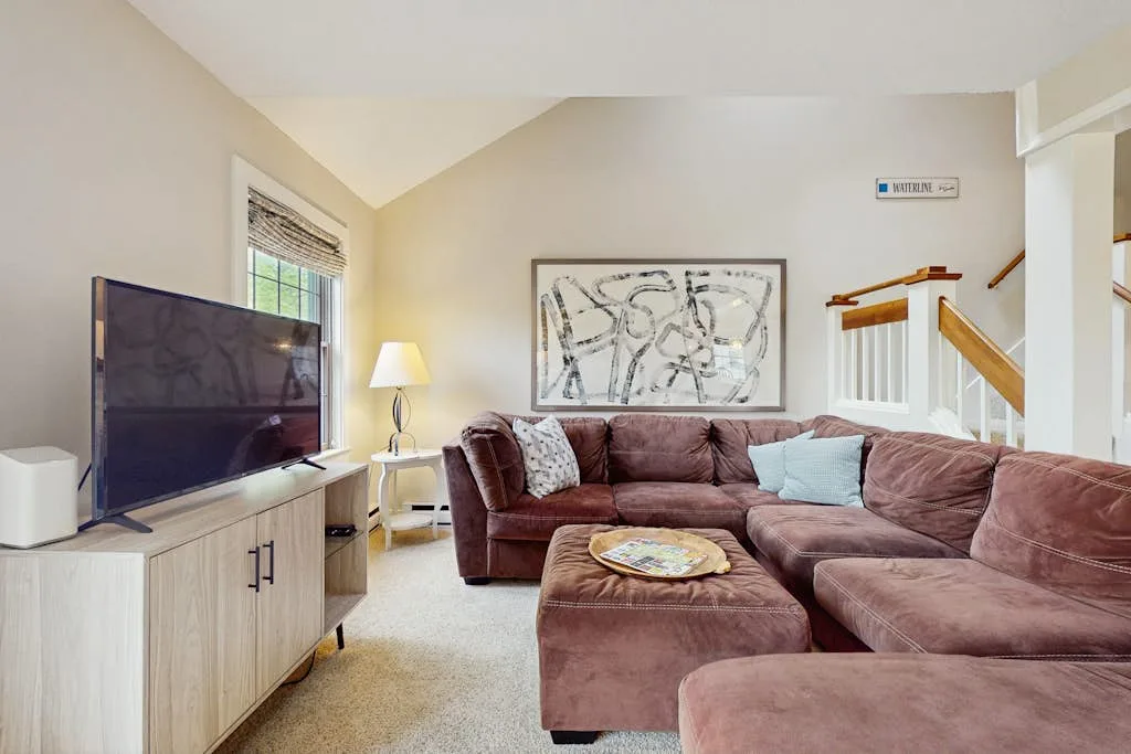 A living room with sectional seating, a television, and a staircase.