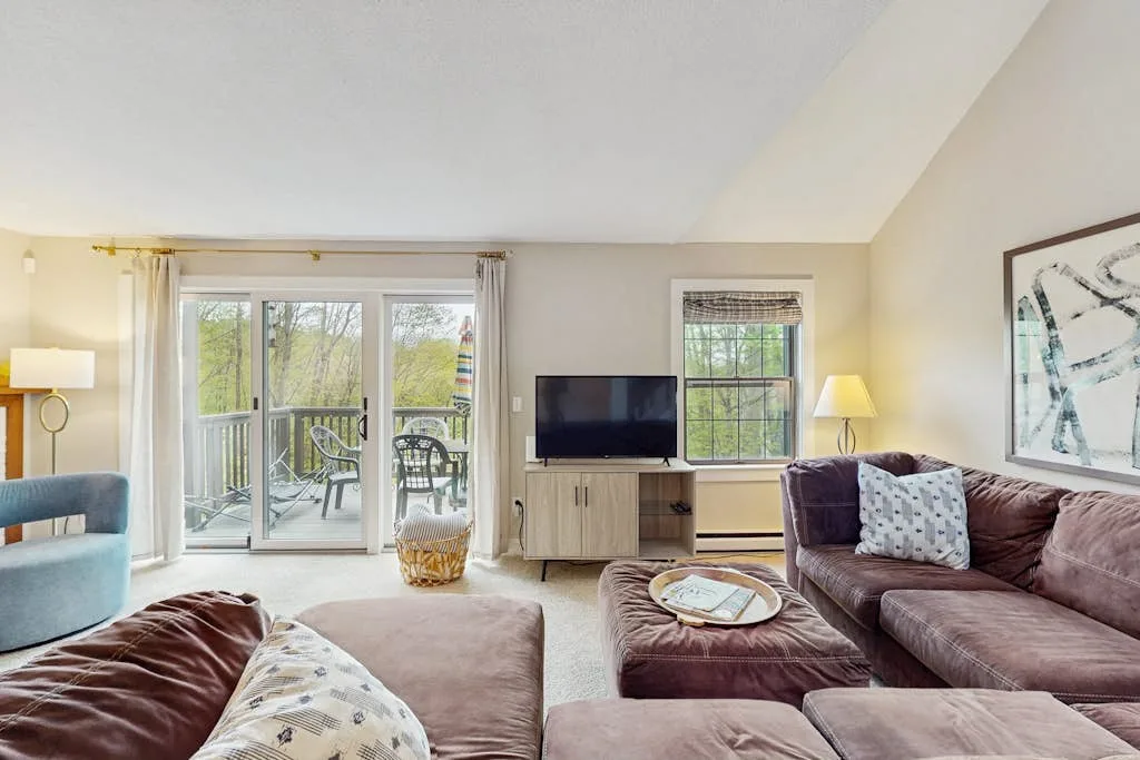 A bright living room with seating, a television, and glass doors opening to a balcony.