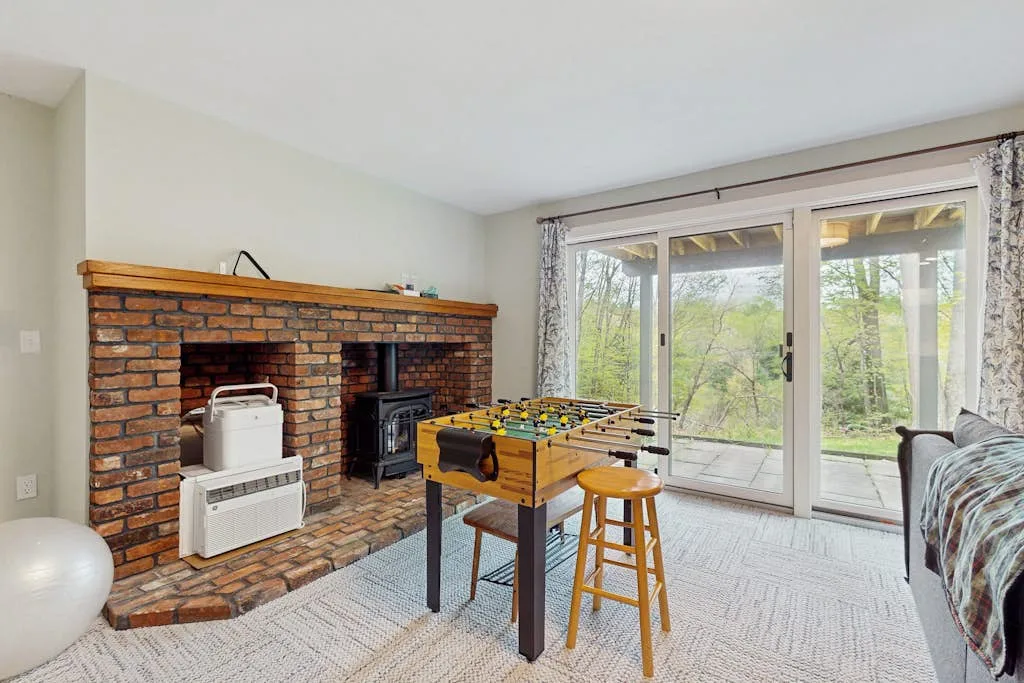 A recreation room with a foosball table, brick fireplace, and glass doors.