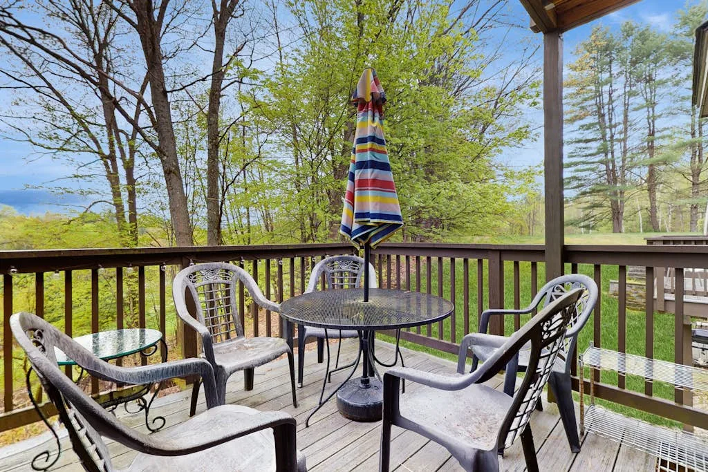 A deck with outdoor seating and a striped umbrella overlooks a wooded landscape.