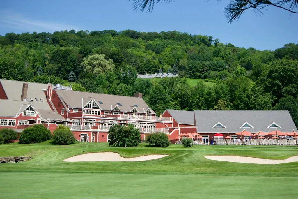 A large red building stands beside a green lawn, with wooded hills behind it.