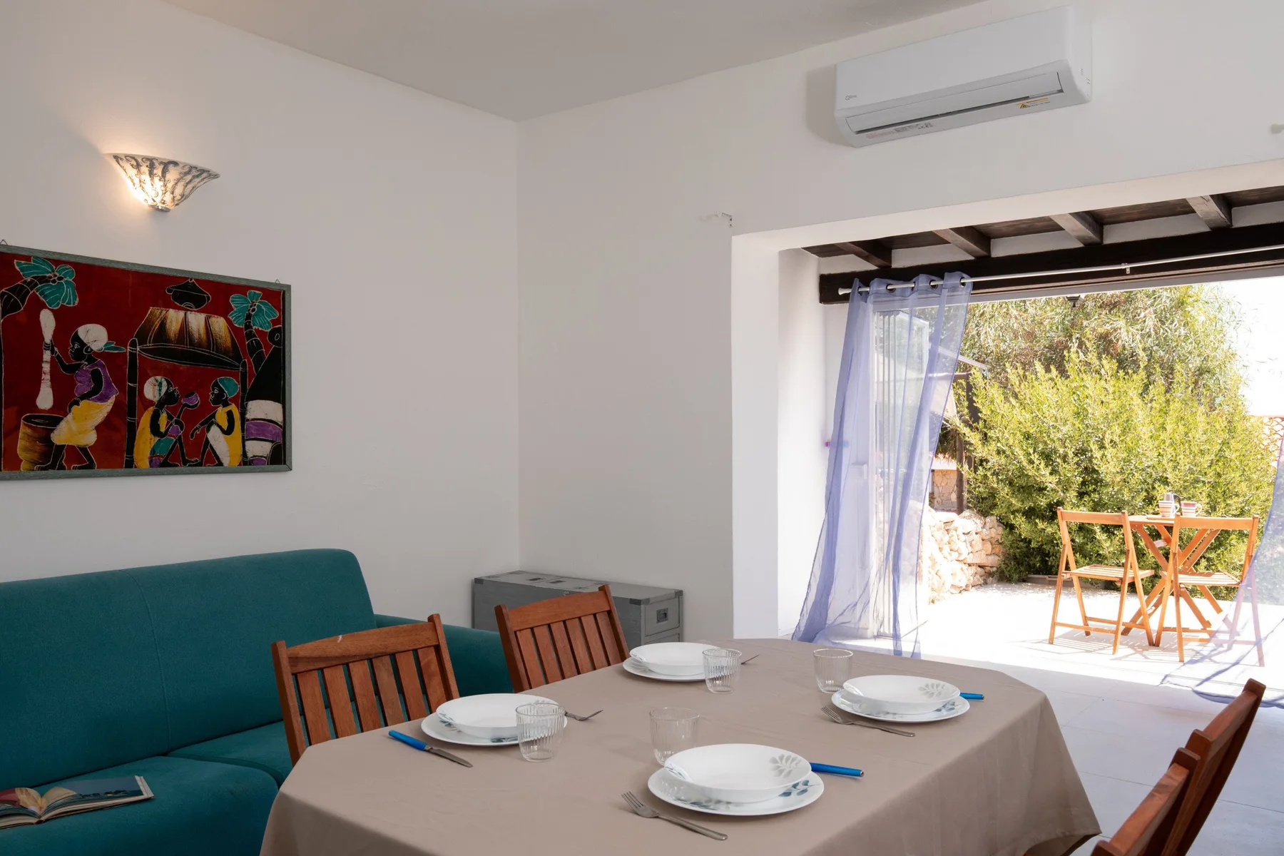 A dining table is set beside teal seating and an open doorway to a patio.