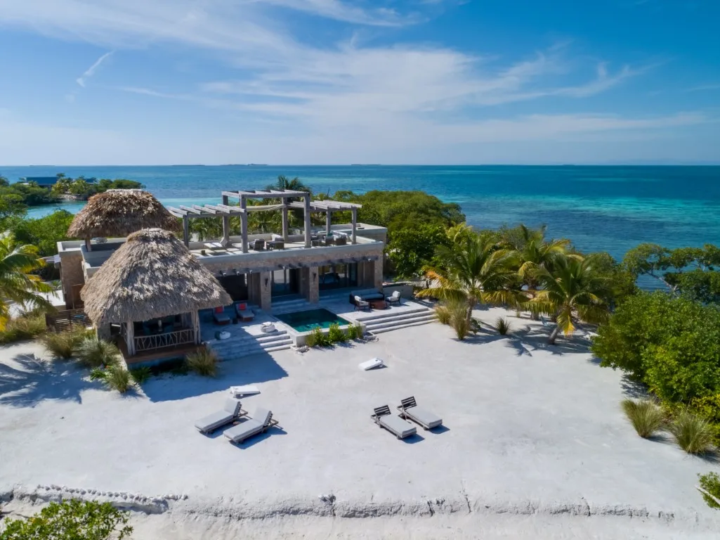 A beachfront resort with a pool and lounge chairs faces the turquoise sea.