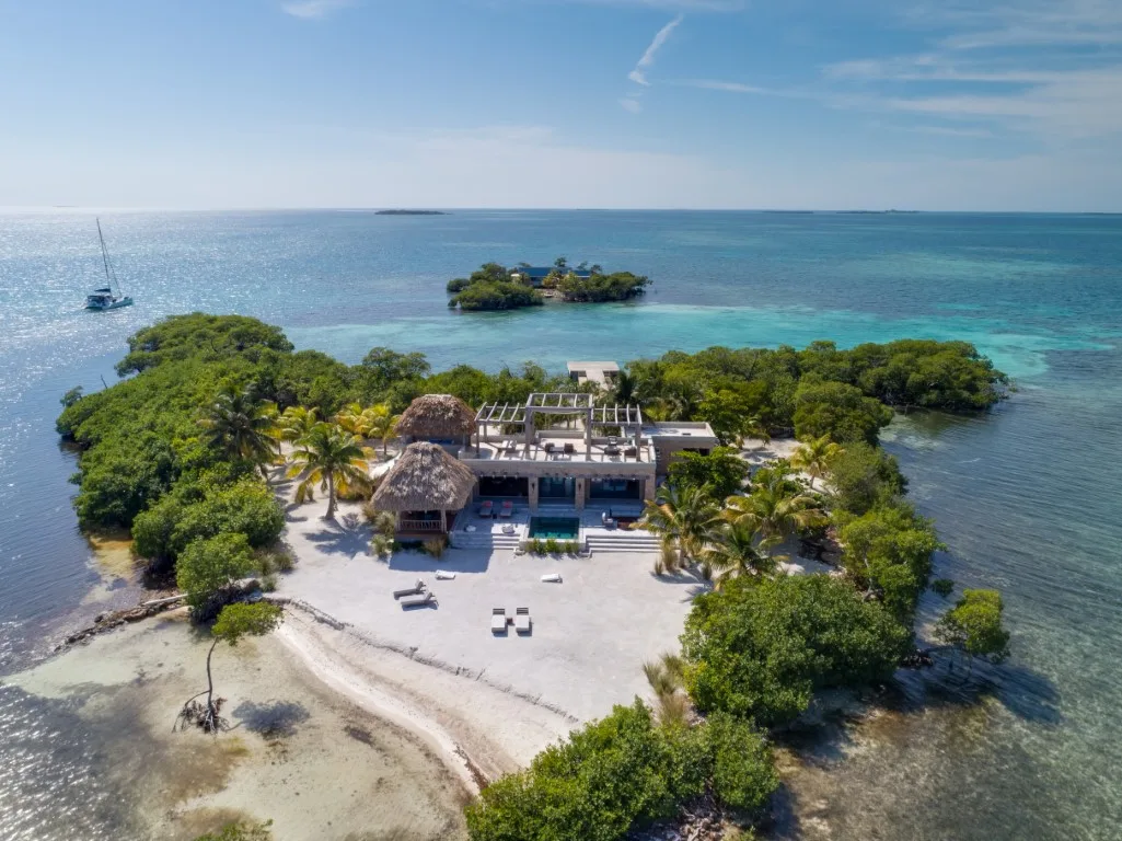 An aerial view of a beachfront building surrounded by trees and clear water.
