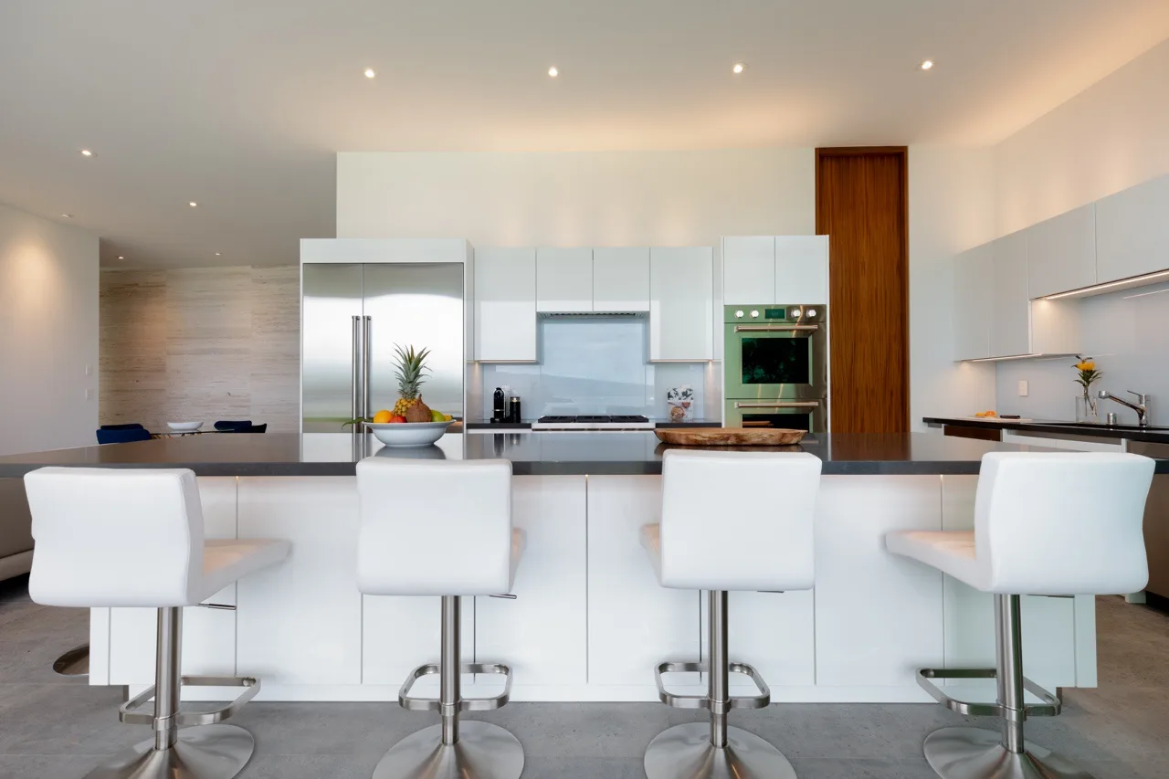 A modern kitchen with white cabinetry and a long island lined with seating.