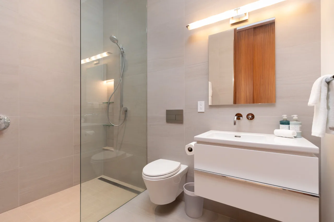 A modern bathroom with a glass shower, toilet, and sink.