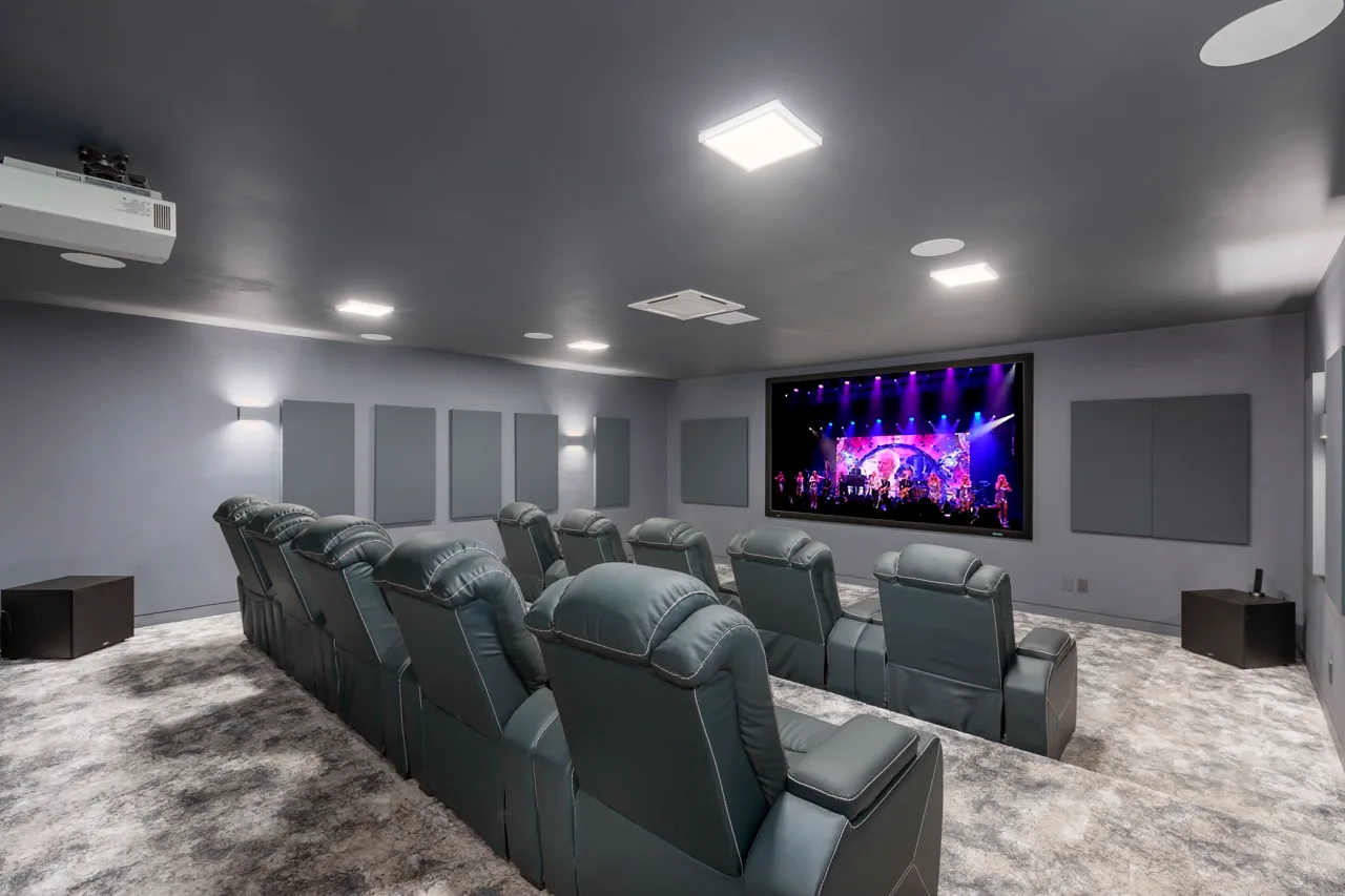 Una sala de cine en casa con filas de asientos reclinables frente a una pantalla grande.