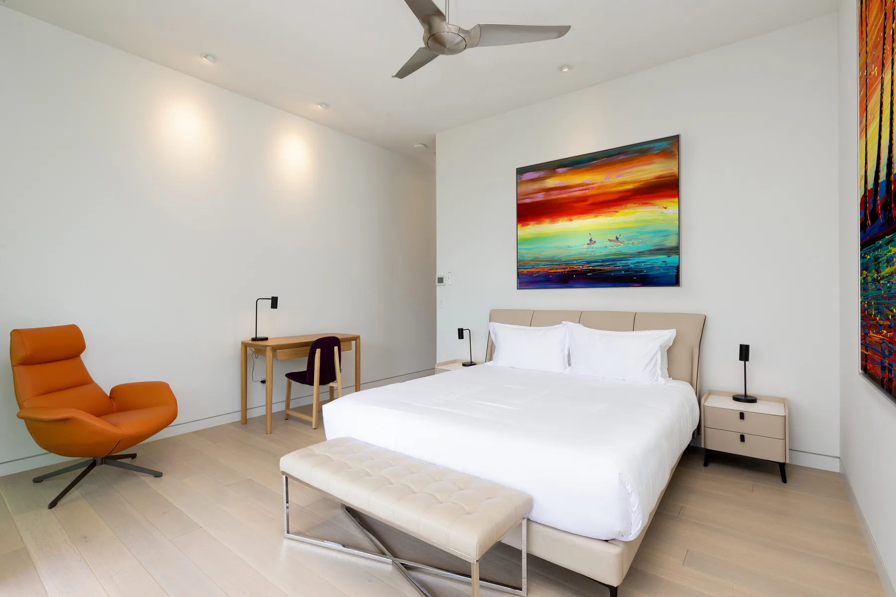 A bright bedroom with a neatly made bed and colorful artwork on the wall.