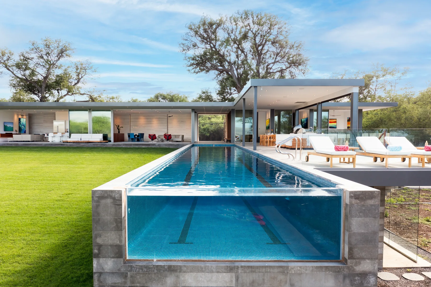 A modern house and swimming pool bordered by a broad green lawn.