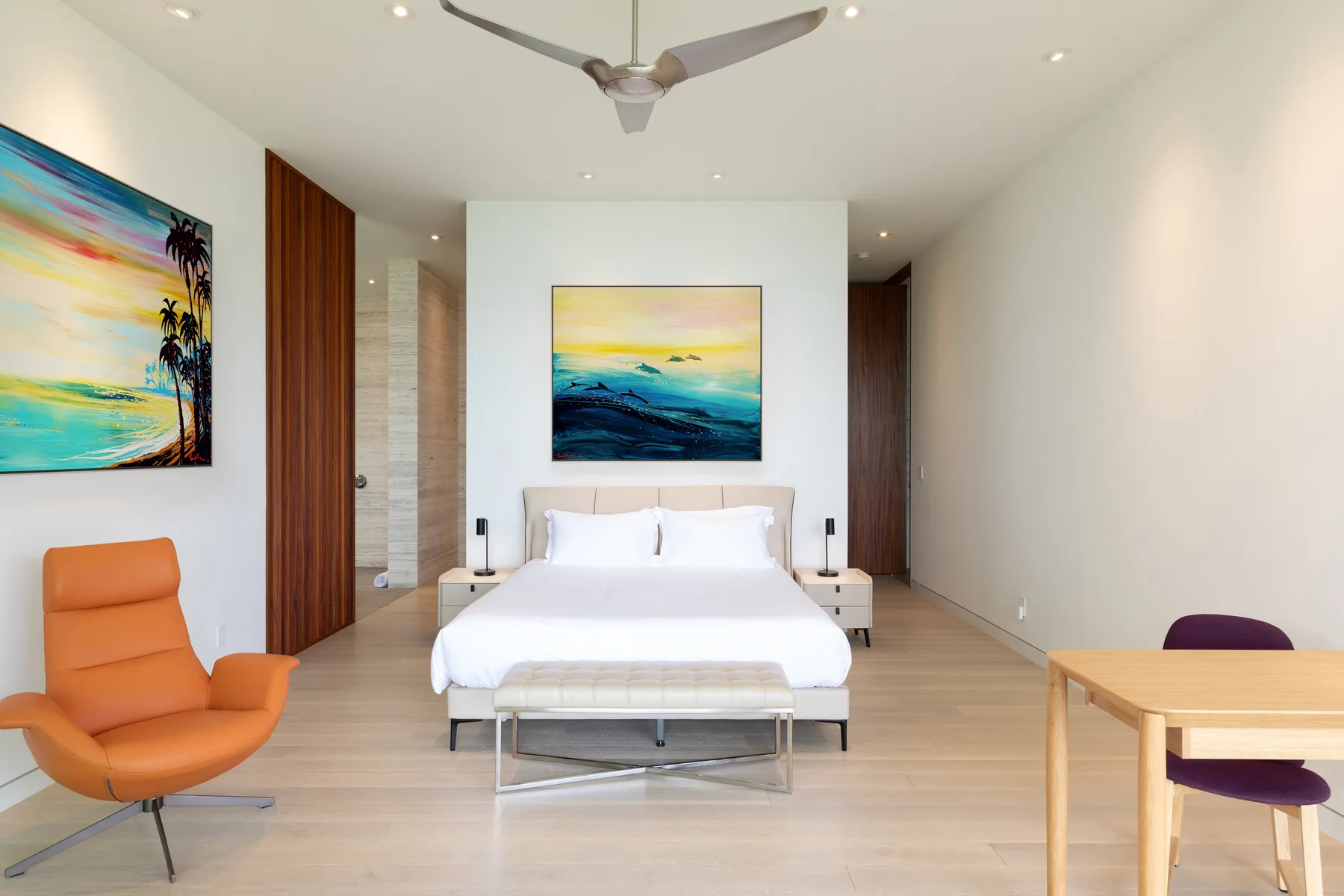 A bright bedroom with a white bed, colorful artwork, and seating.