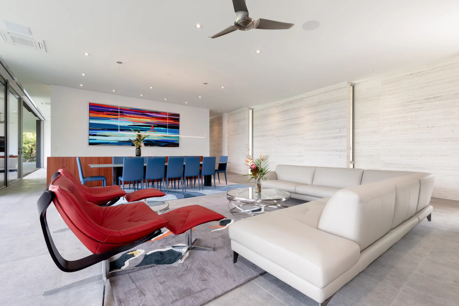 A modern living and dining area with a white seating area and red lounge chairs.