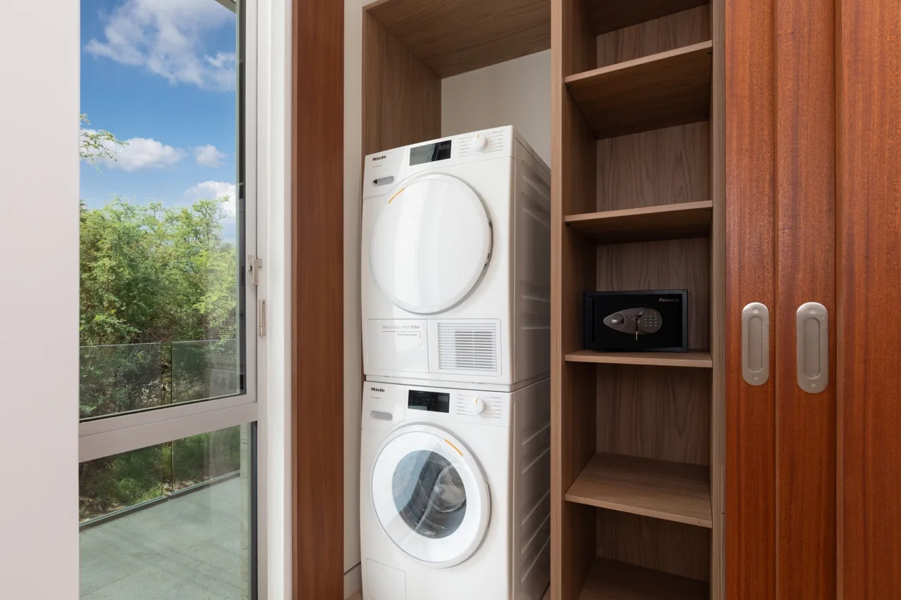 A laundry area with a stacked washer and dryer beside open shelving and a window.