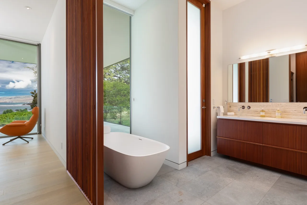 A bathroom with a freestanding bathtub and a long vanity beside a glass door.