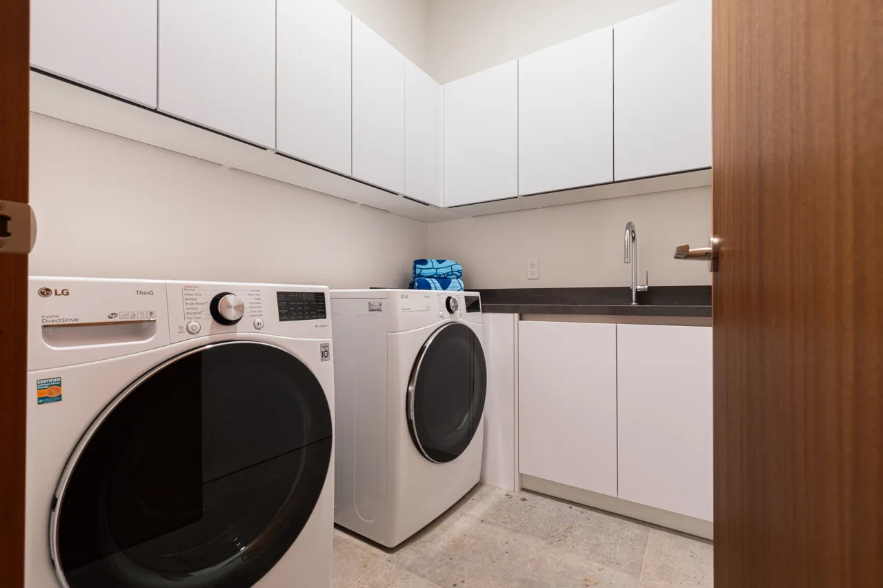A laundry room with front-loading machines, white cabinets, and a countertop.