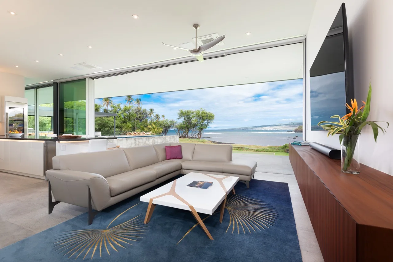 A bright living room opens onto a wide ocean view, with seating and a low table.