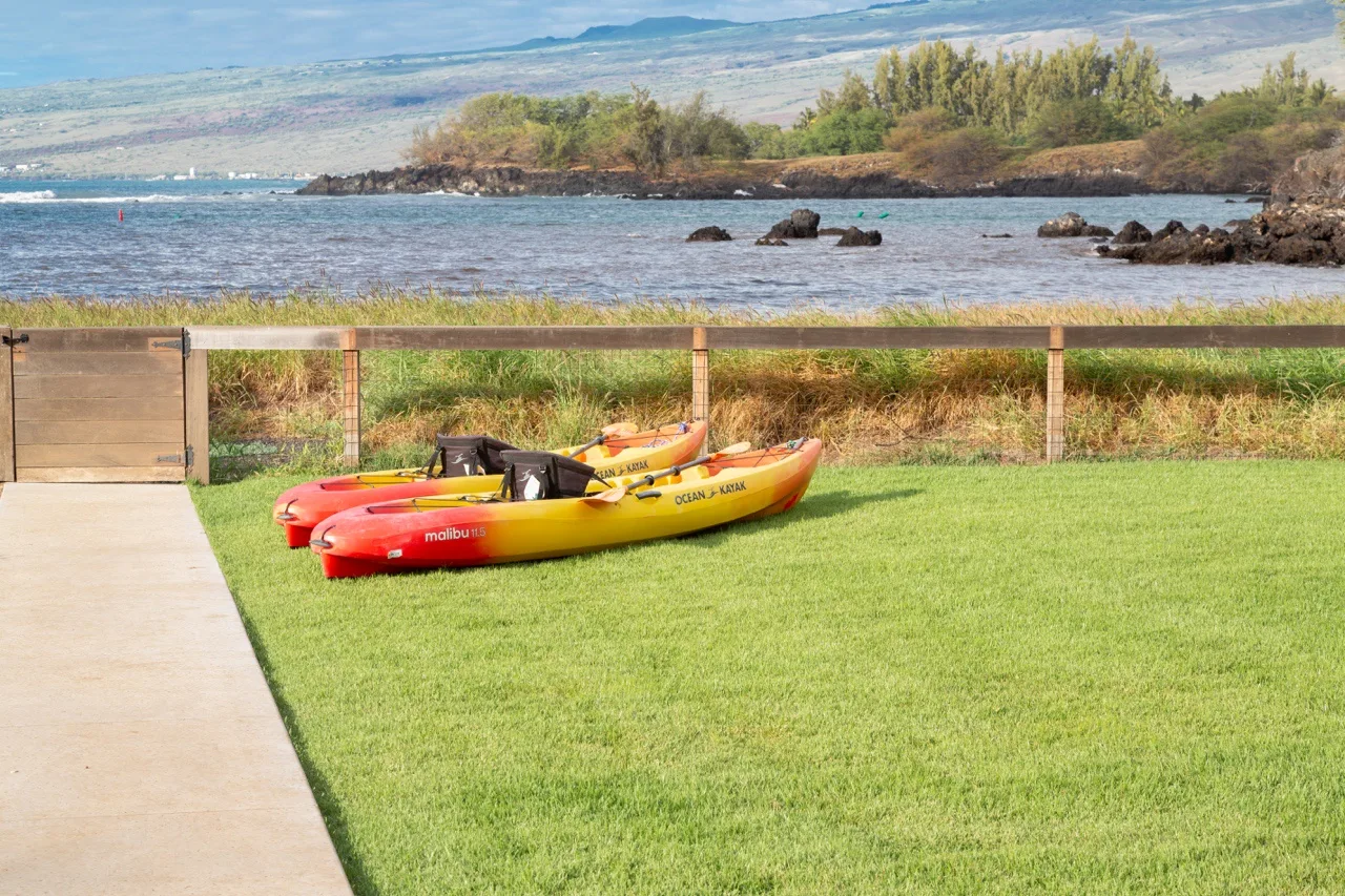 A grassy waterfront area with kayaks beside a paved path.