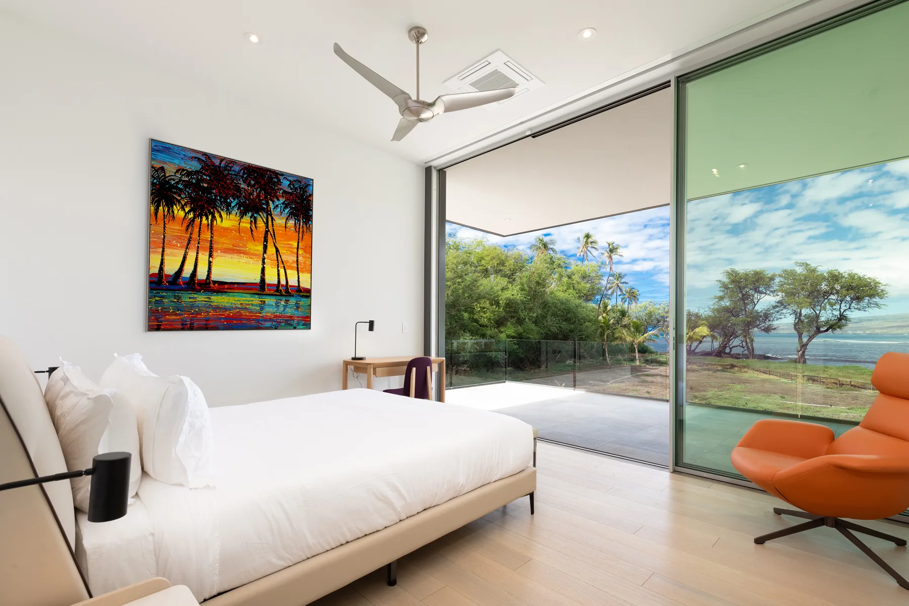 A bedroom with a bed beside large glass doors opening onto a green view.