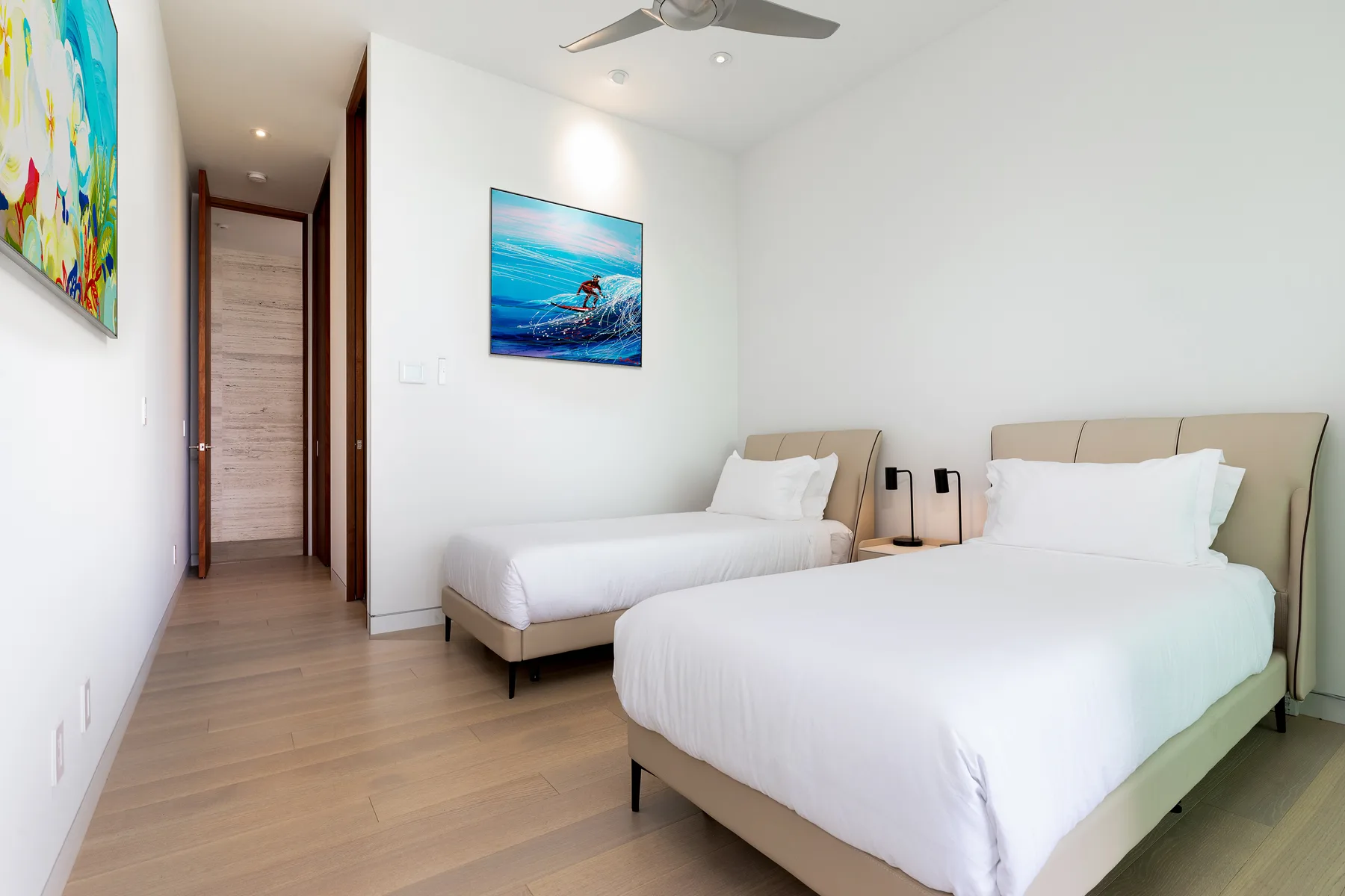 A bright bedroom with two beds and colorful artwork on the walls.
