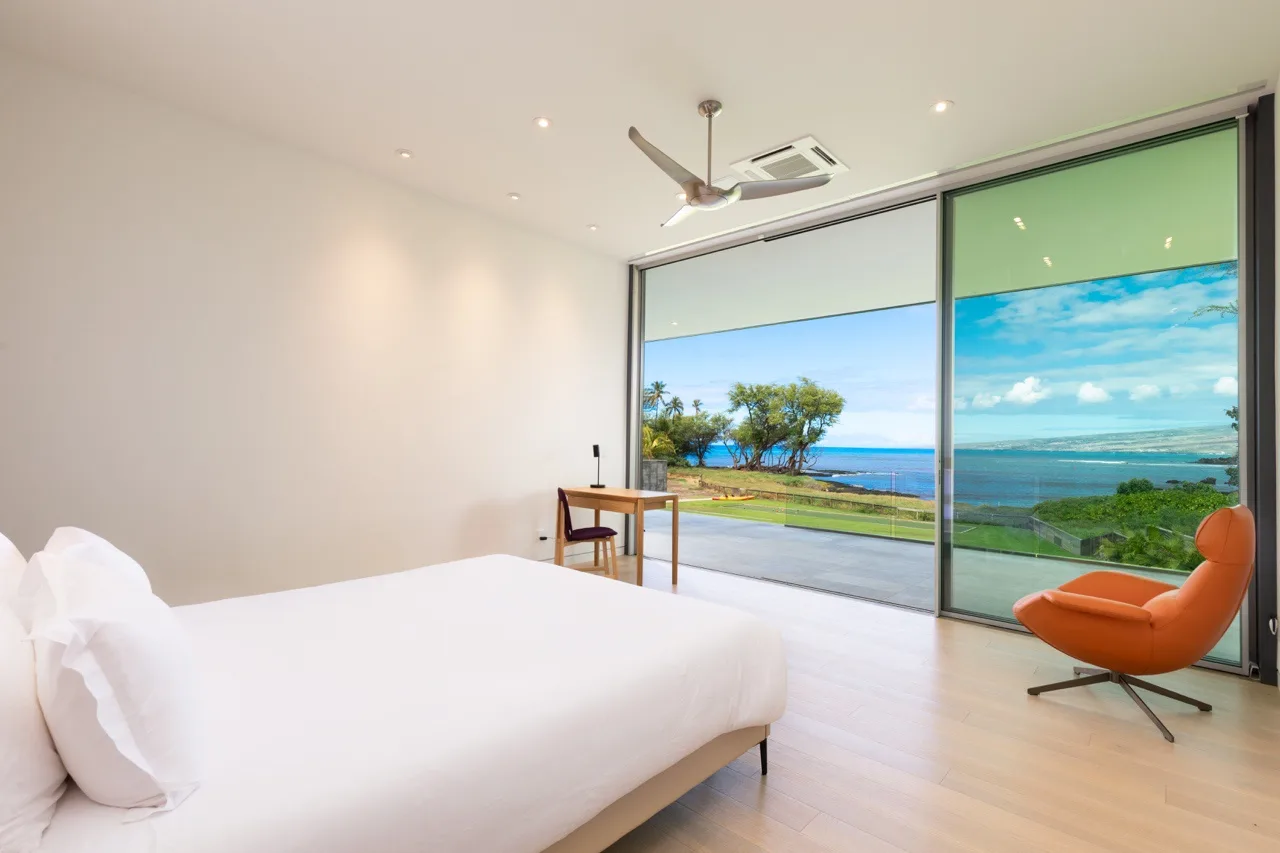 A bedroom with a bed and floor-to-ceiling windows overlooking the ocean.