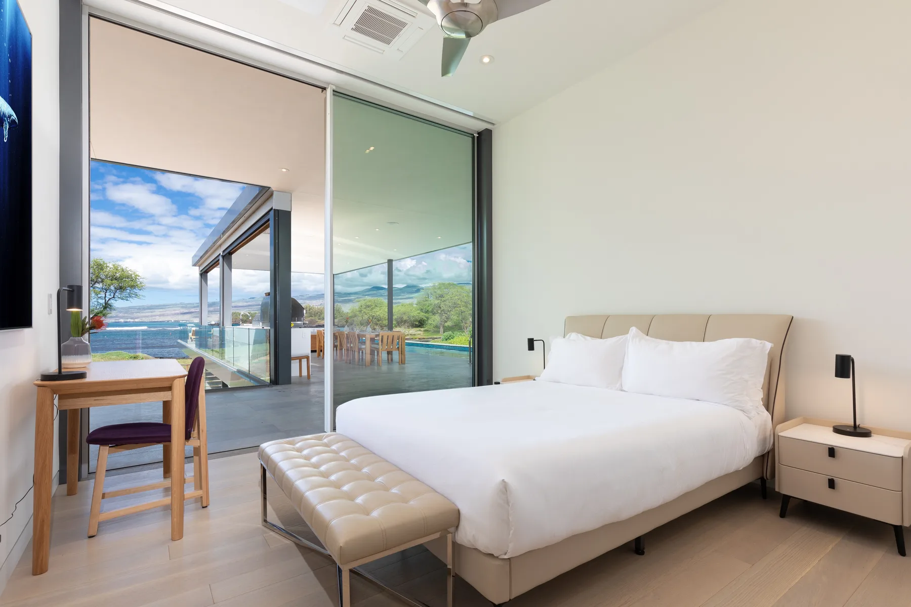 A bedroom with a neatly made bed beside floor-to-ceiling glass doors overlooking a terrace.