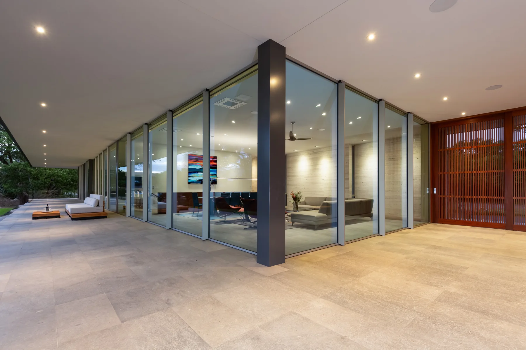 A glass-walled living room opens onto a covered patio with outdoor seating.