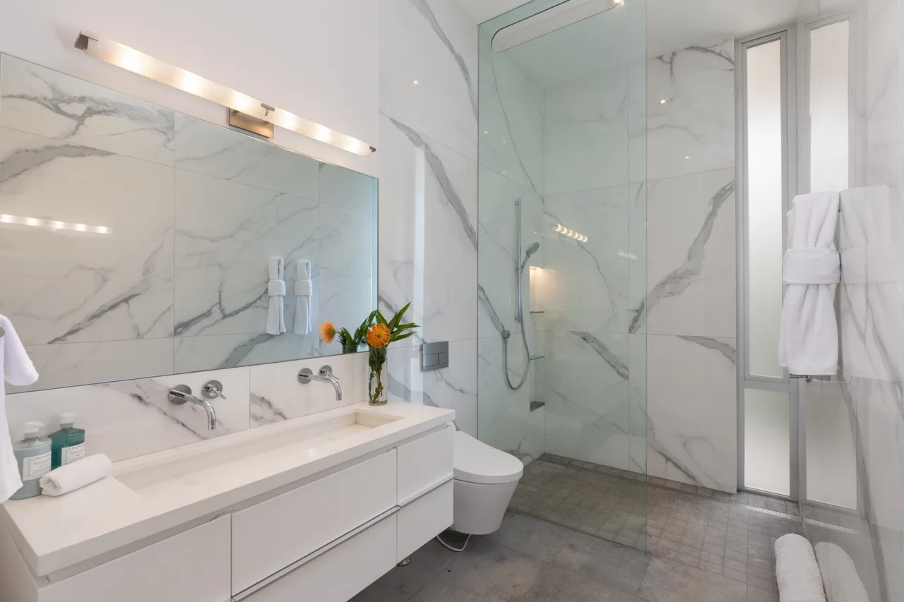 A bright bathroom with a long vanity, large mirror, and glass shower.