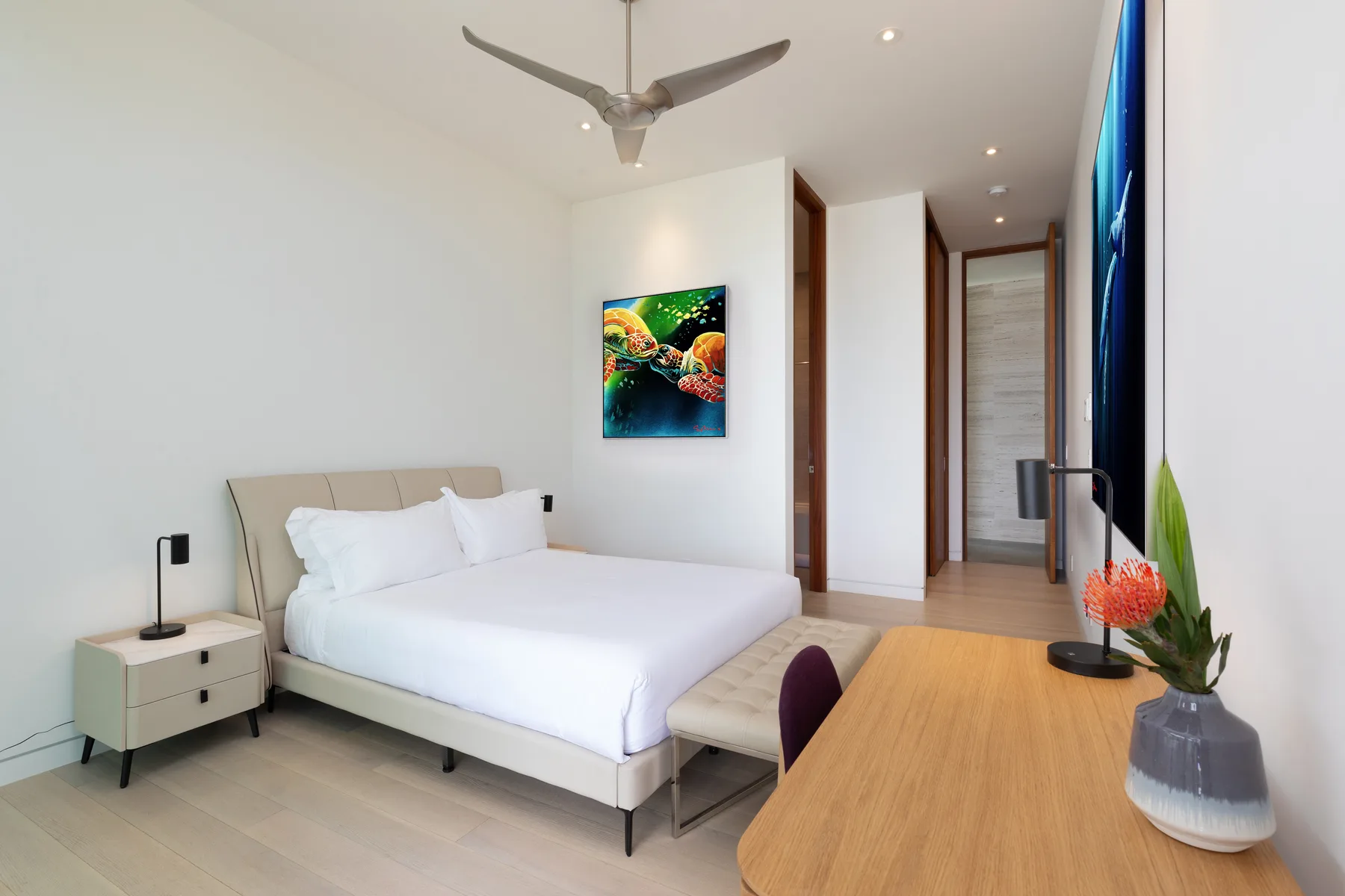 A bright bedroom with a neatly made bed, bedside table, and ceiling fan.