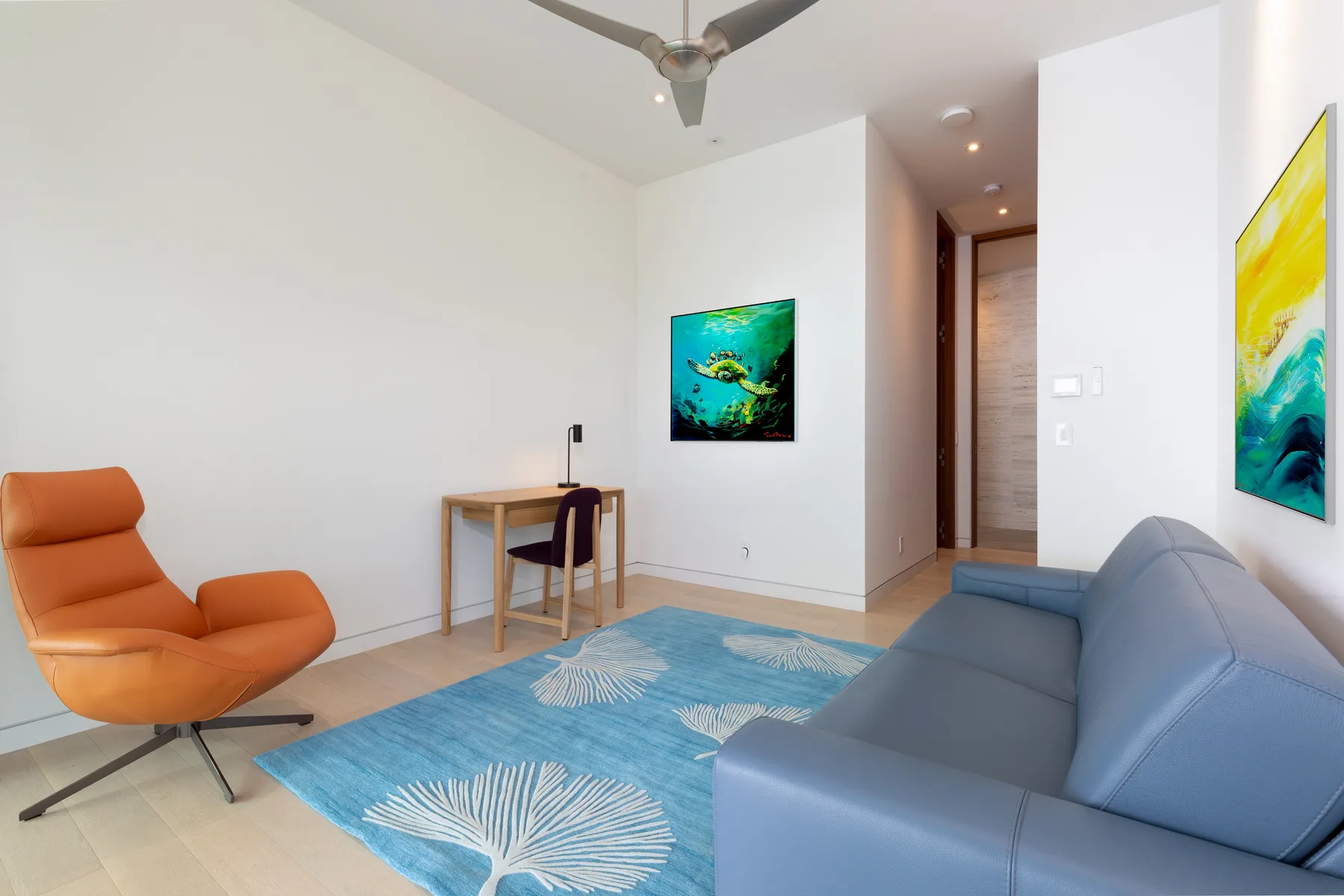 A bright living room with seating, a small desk, and a blue area rug.