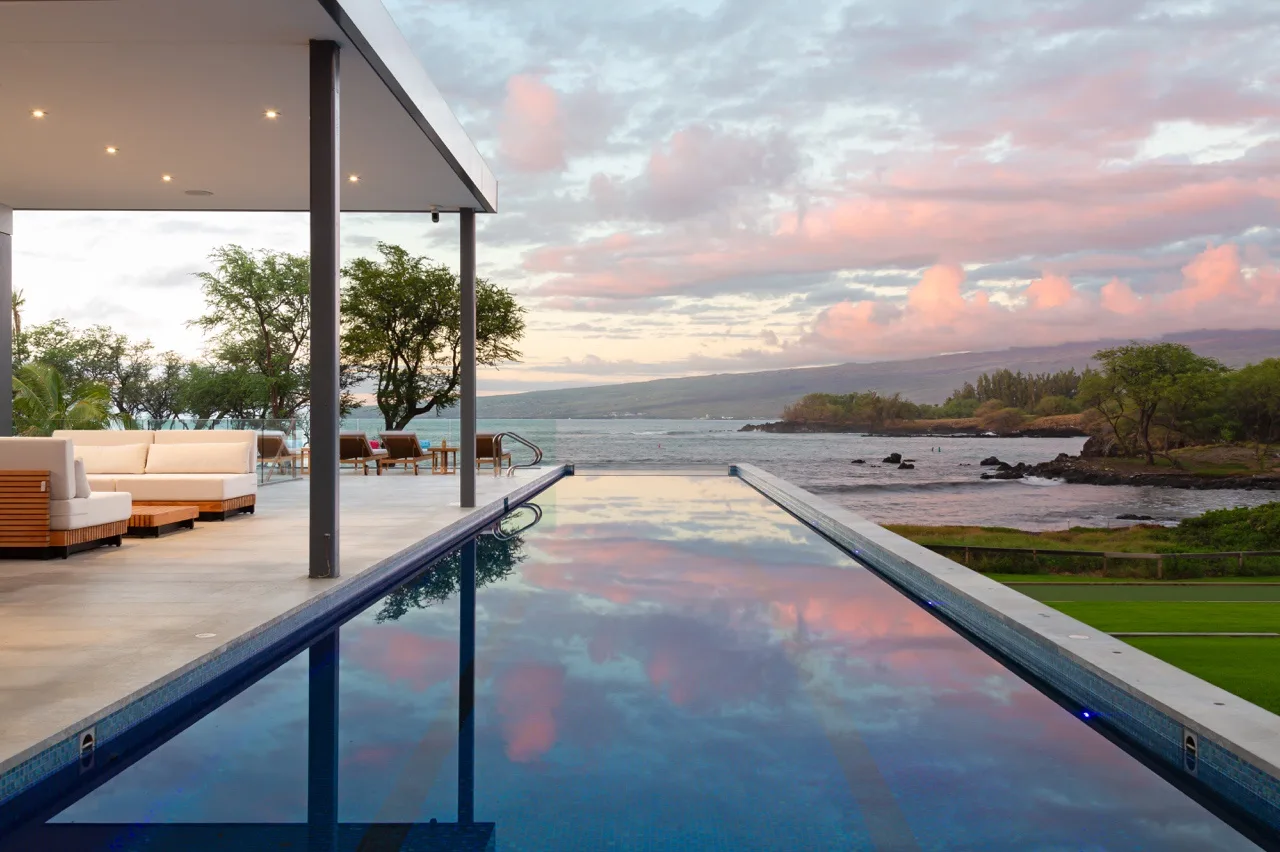 Una piscina al aire libre mira hacia el agua bajo un cielo colorido al atardecer.