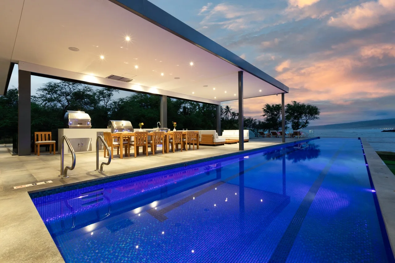 Una piscina al aire libre junto a un comedor cubierto al atardecer.