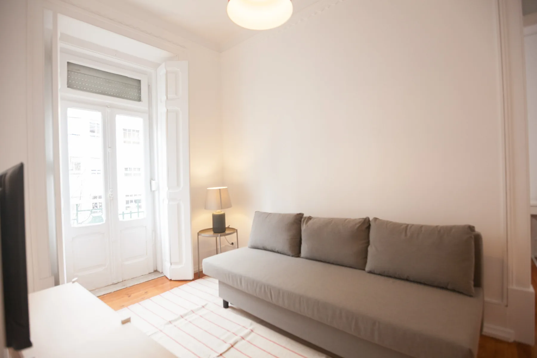 Una sala luminosa tiene un sofá junto a ventanas altas y una mesita auxiliar.