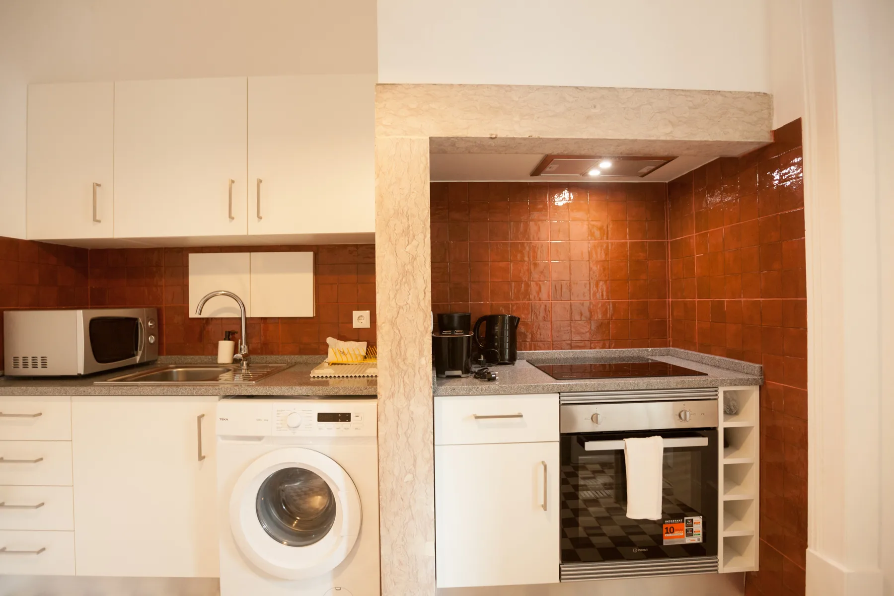 Una cocina compacta con armarios blancos, una lavadora y una placa de cocina integrada.