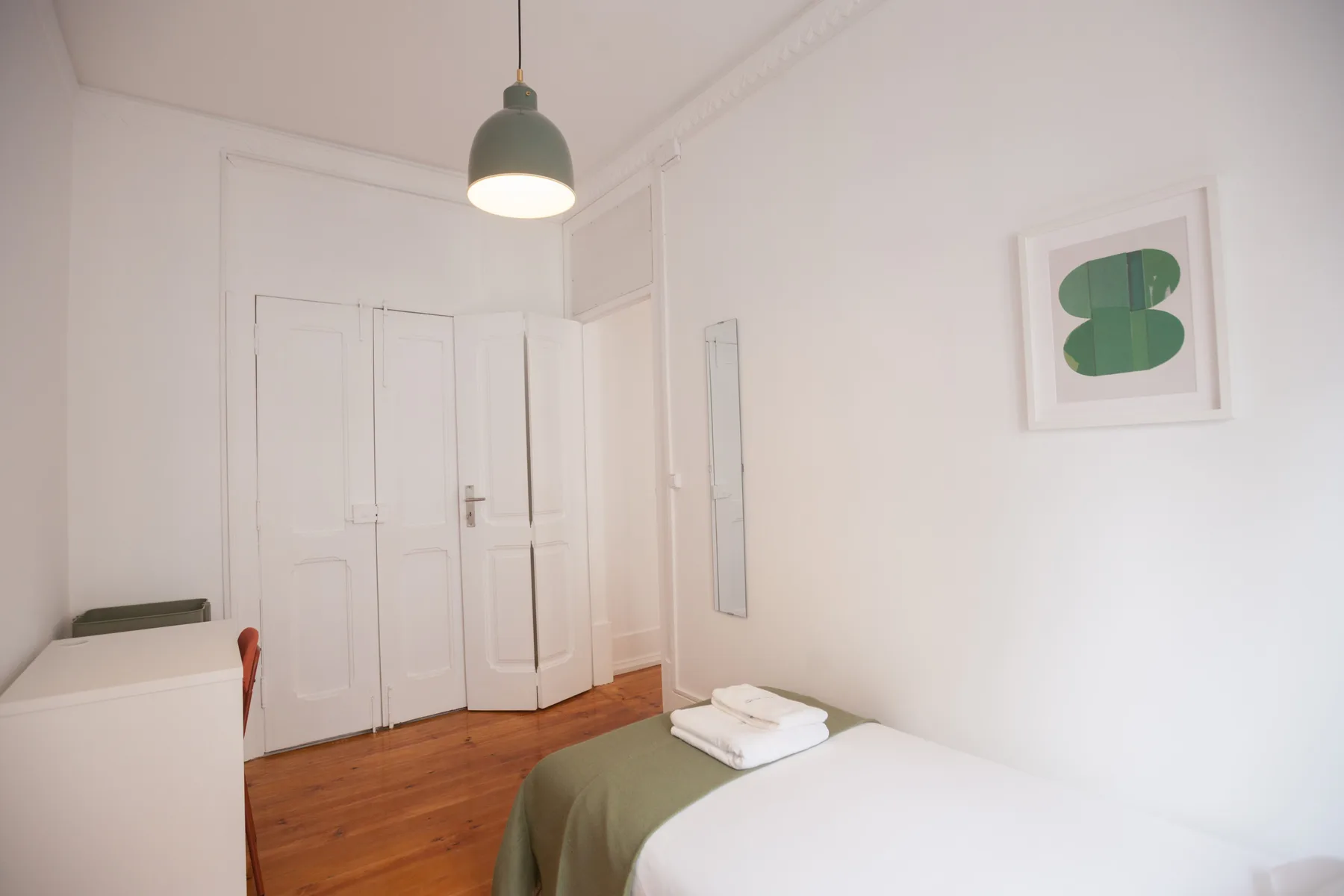Un dormitorio con una cama, toallas dobladas y puertas blancas con paneles.