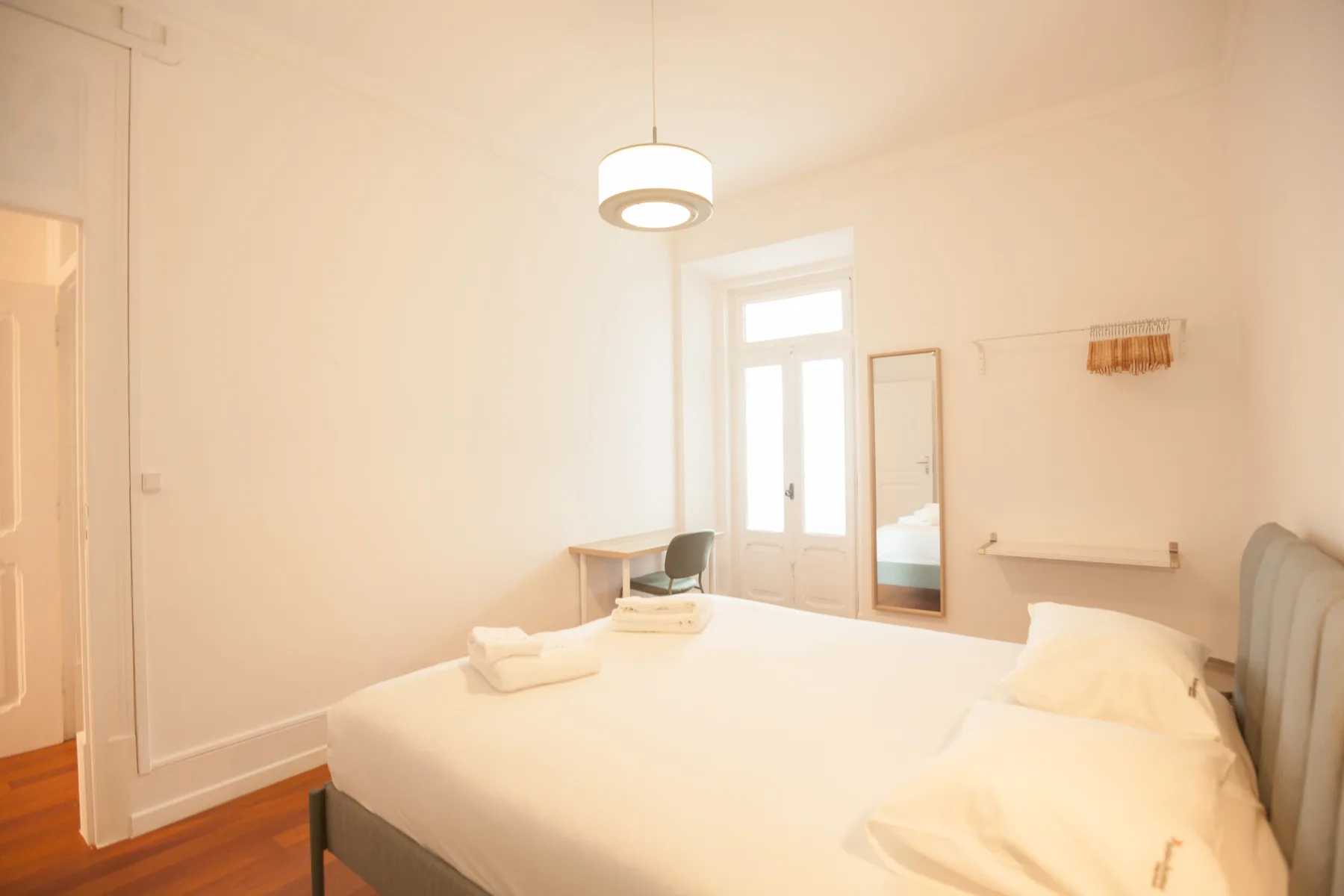 Un dormitorio luminoso con una cama, un escritorio y ventanas altas.