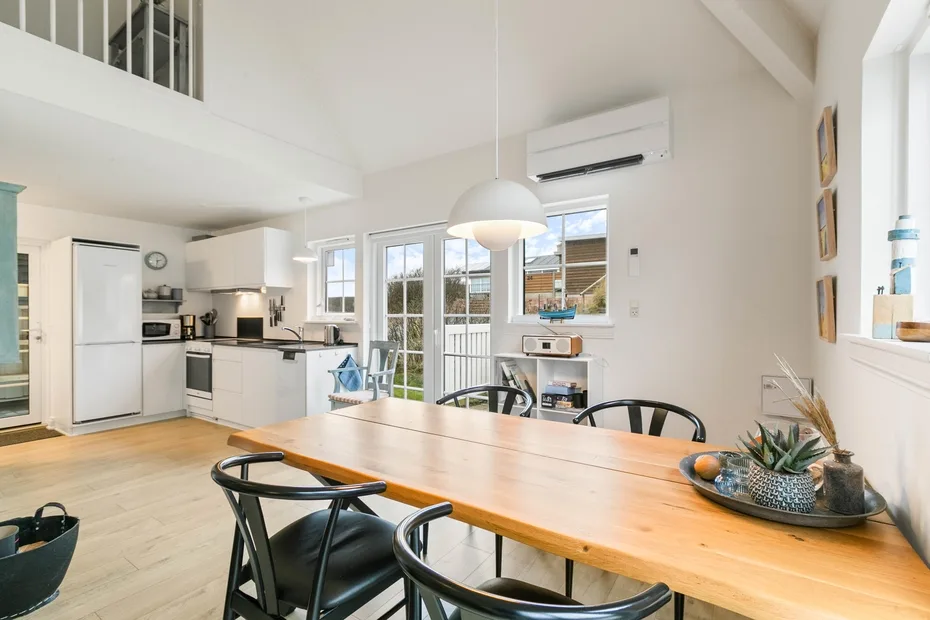 Una luminosa cocina-comedor de espacio abierto con una mesa de madera y ventanas amplias.