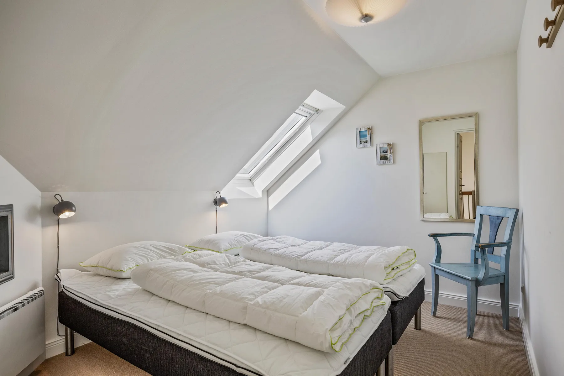 Un dormitorio abuhardillado y luminoso tiene dos camas bajo un techo inclinado y una claraboya.