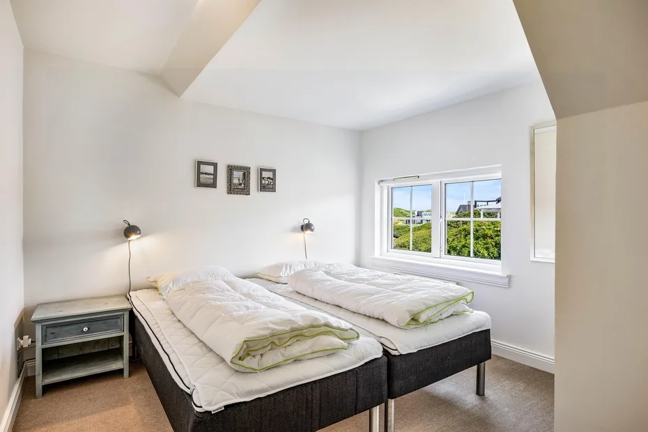 Un dormitorio luminoso con dos camas y una ventana con vistas a zonas verdes.
