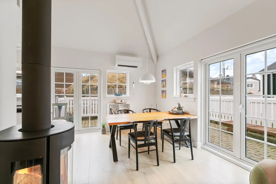 Un comedor luminoso con una mesa de madera junto a grandes ventanas y puertas de vidrio.