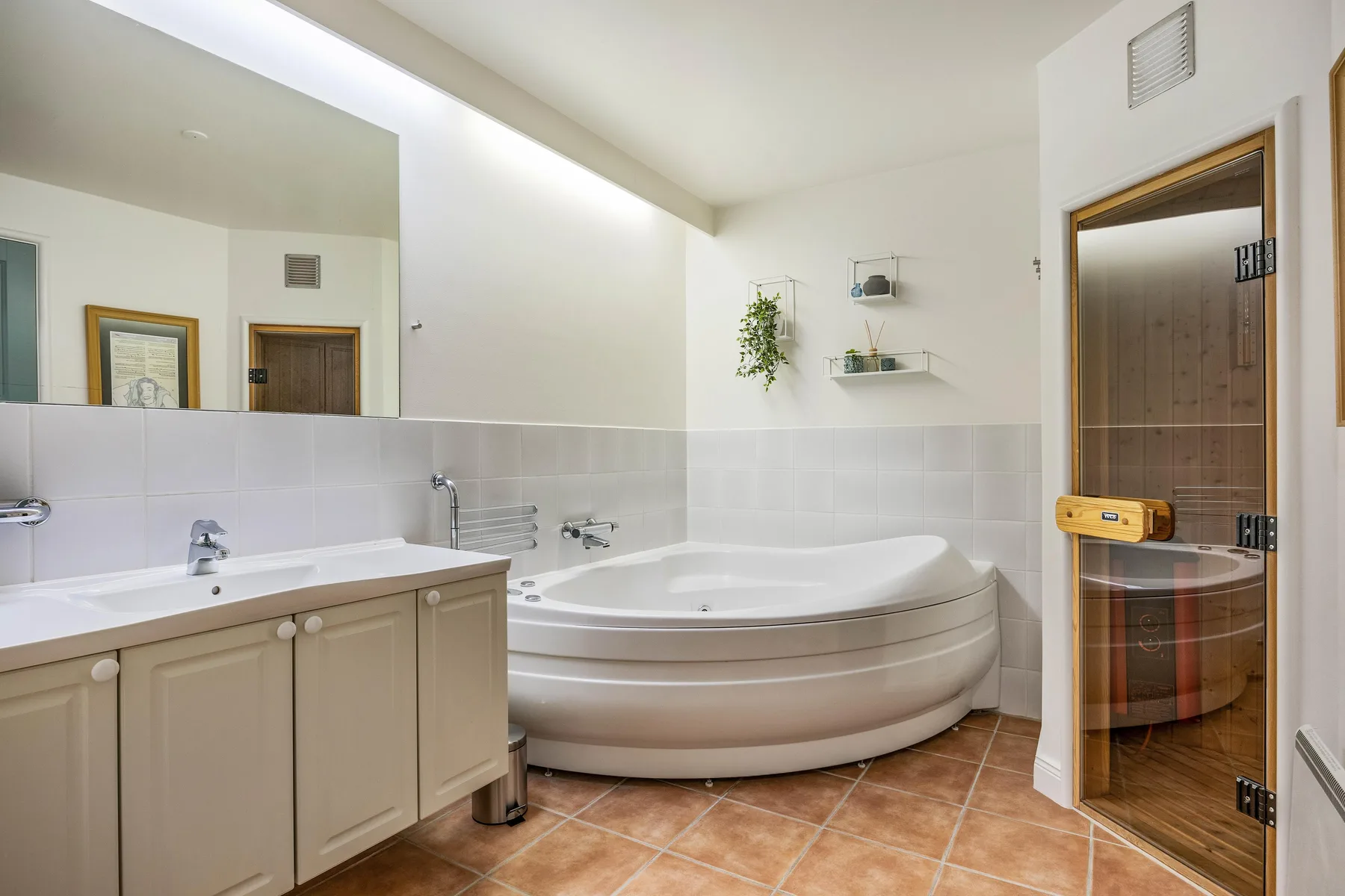 Un baño luminoso con bañera de esquina, tocador y sauna con frente de vidrio.