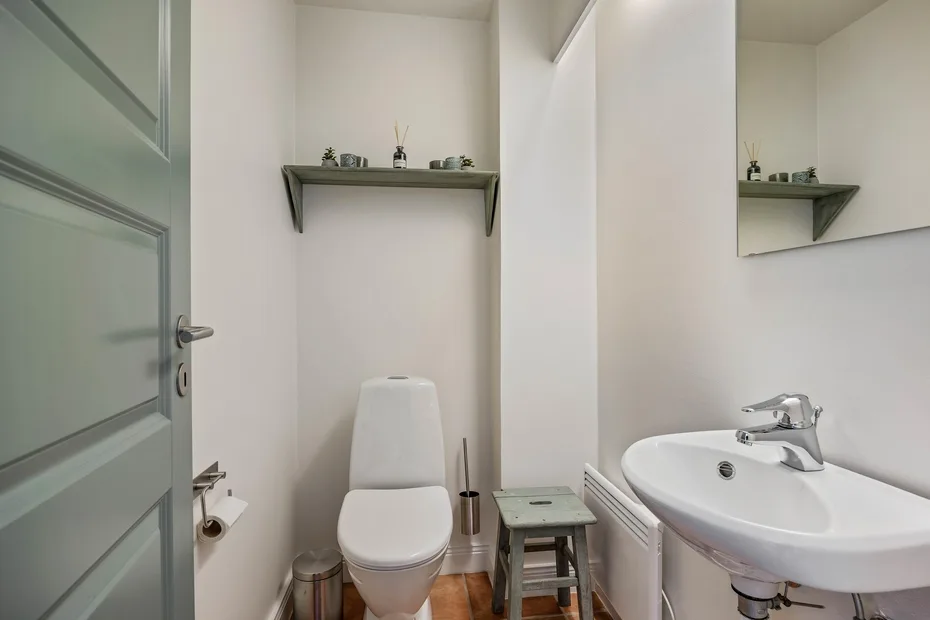 Un baño compacto con inodoro, lavabo y una pequeña repisa en la pared.