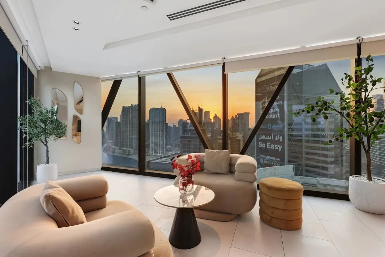 Una sala de estar moderna con asientos y ventanales con vistas a la ciudad al atardecer.